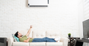 Man on a couch using a remote to control his ductless HVAC unit
